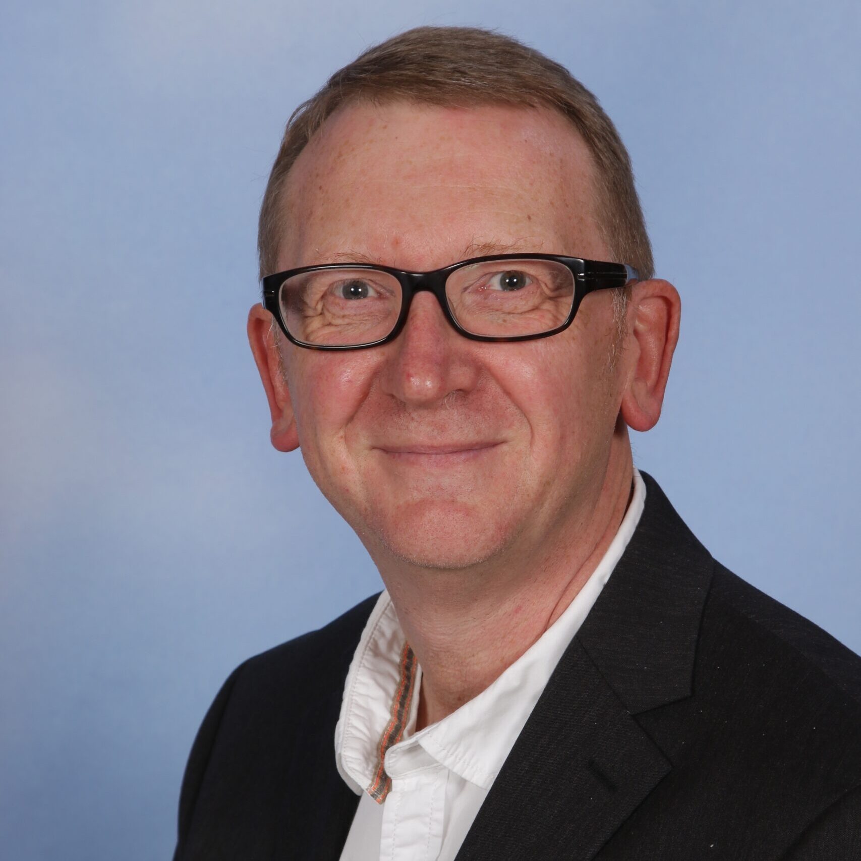 Porträt von Claus Schilke in einem weißen Hemd und schwarzen Jackett.
