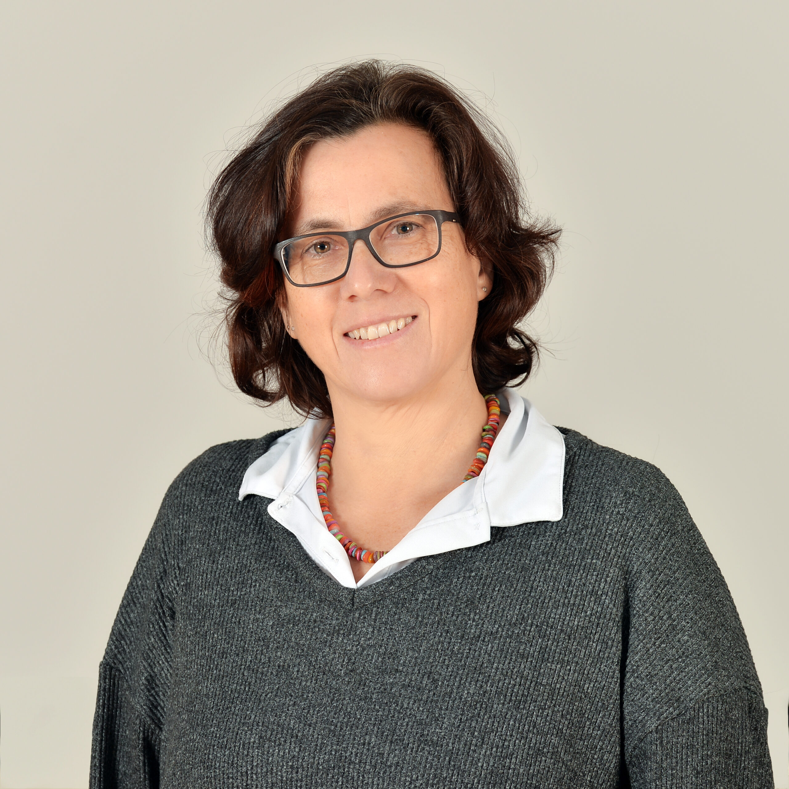 Profilbild von Sabine Carstens in einer weißen Bluse und grauem Pullover.
