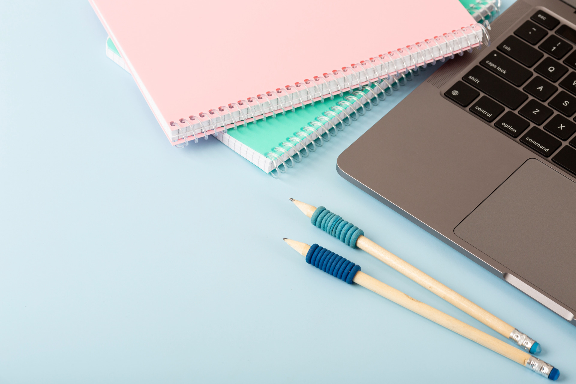 Ein Laptop und zwei Notizbücher im Anschnitt. Davor liegen zwei Stifte.