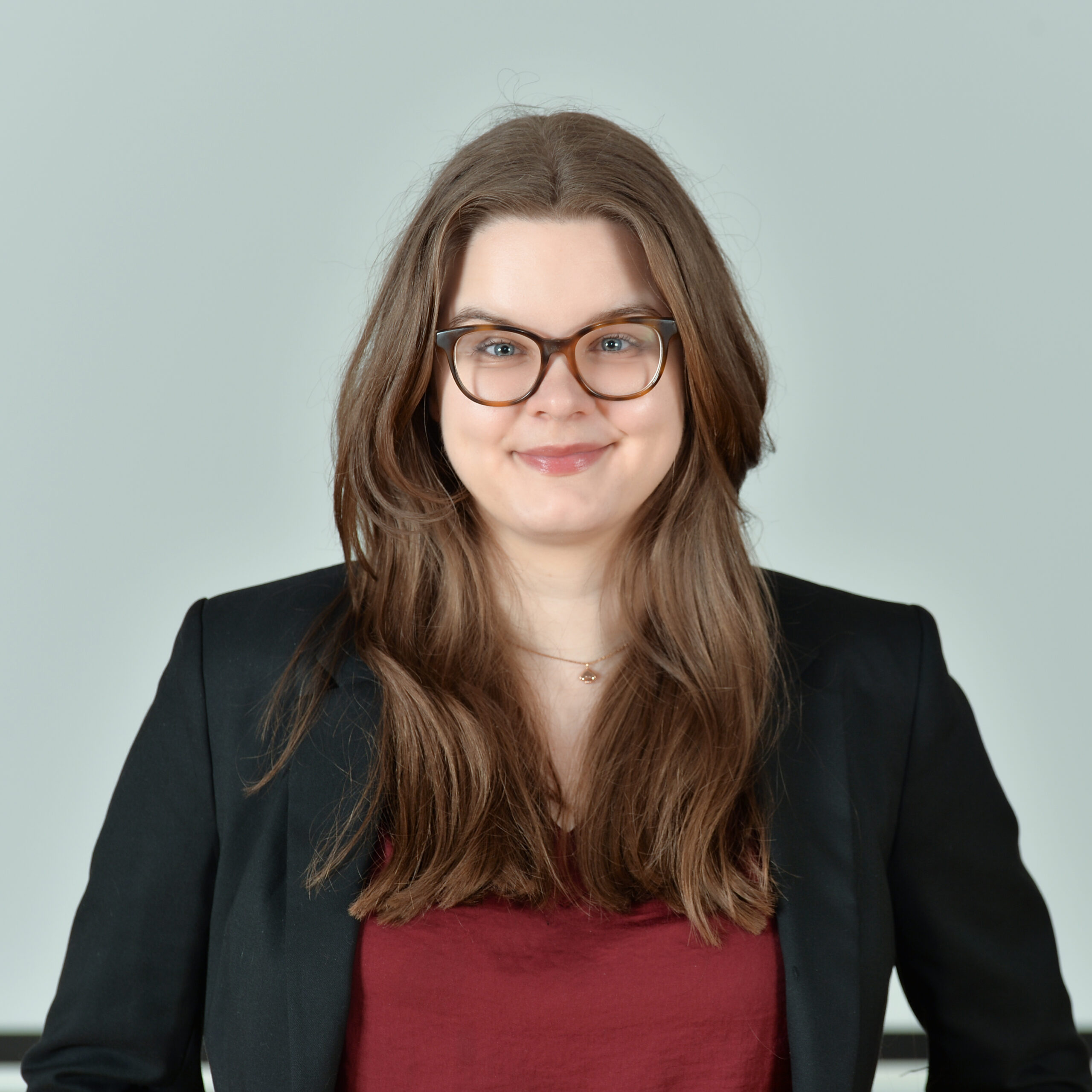 Profilbild von Annemarie Pläschke in einem dunkelroten Top und dunkelgrauen Blazer.